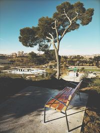 Empty bench by tree against sky in city