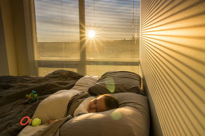 Baby boy sleeping on bed at home during sunrise