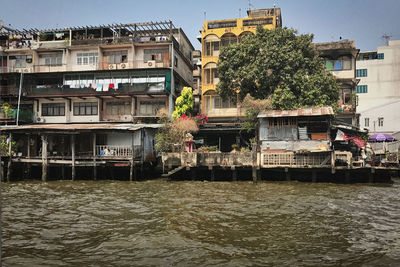 Buildings by river against sky in city