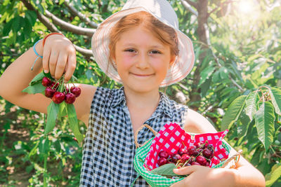 Portrait of smiling girl holding cherries against tree