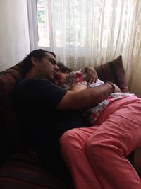 Son embracing mother while sleeping on sofa at home