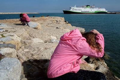 People on rock by sea against sky