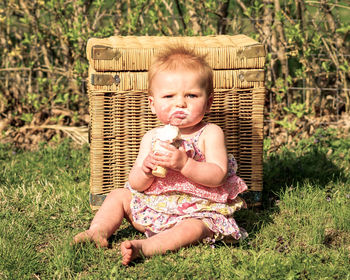 Portrait of cute baby girl eating ice cream while sitting on grassy field in park