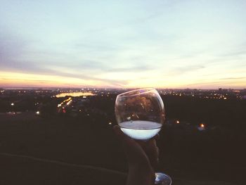 Close-up of hand holding drink against sky during sunset