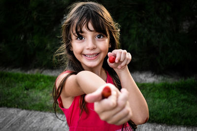 Portrait of smiling girl holding red berries while standing on footpath