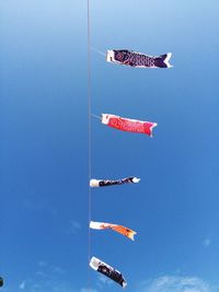 Low angle view of windsocks blowing in wind against clear blue sky