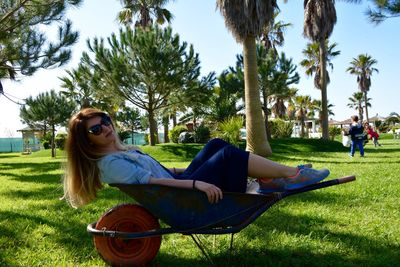 Smiling young woman sitting on wheelbarrow at park