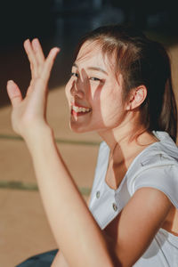 Portrait of smiling young woman shielding eyes while sitting on floor