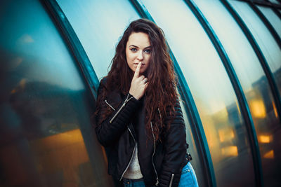 Portrait of young woman with finger on lips standing on street in city