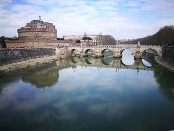 Arch bridge over river by buildings against sky