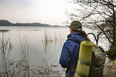 Rear view of man standing by lake against trees