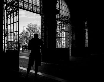 Rear view of silhouette man standing by window in building