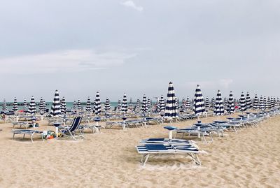 White and blue deck chairs on beach against sky