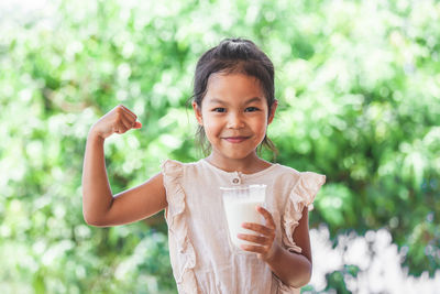 Portrait of smiling girl flexing muscles while holding milk against plants