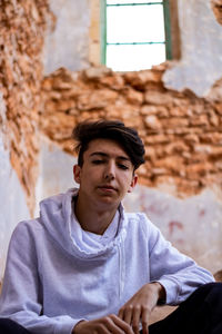 Low angle portrait of young man sitting against wall