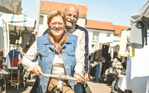 Portrait of smiling couple riding bicycle on road in city