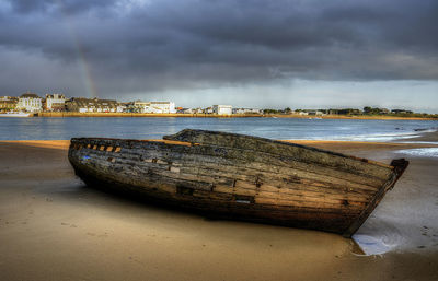 Boat moored at beach against cloudy sky