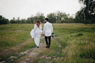 Newlywed couple walking on field against sky