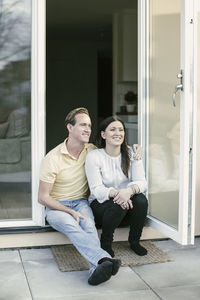 Happy couple looking away while sitting at doorway