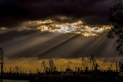 Silhouette cranes against sky at sunset