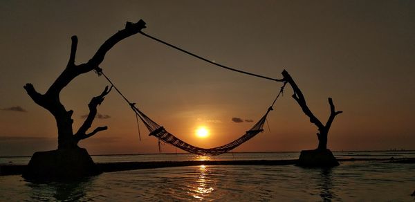 Silhouette tree by sea against sky during sunset