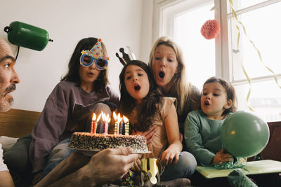 Man holding birthday cake with burning candles in front of surprised family at home