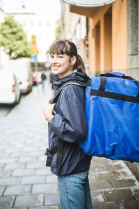 Portrait of confident delivery woman with bag standing on sidewalk