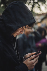 Side view of teenage boy wearing hoodie and using smart phone