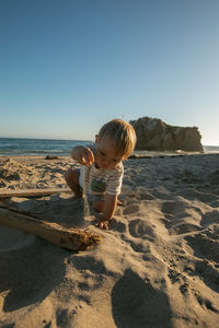 Rear view of girl playing at beach against clear sky
