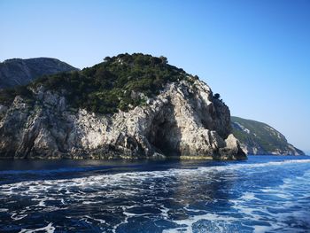 Rock formations by sea against clear blue sky