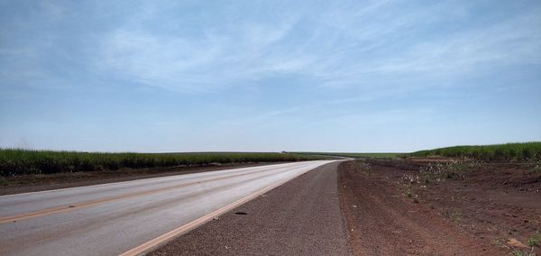 Empty road amidst field against sky