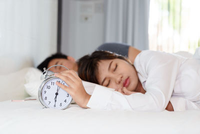 Couple sleeping with alarm clock on bed at home