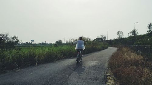 Rear view of man riding bicycle on road against sky