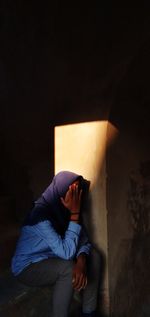 Woman sitting covering face with hand against wall