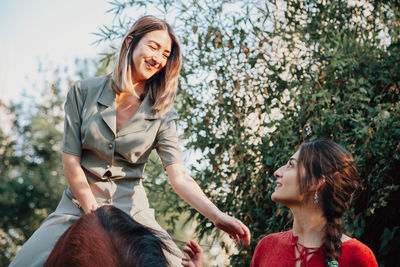 Smiling woman sitting on horse against tree