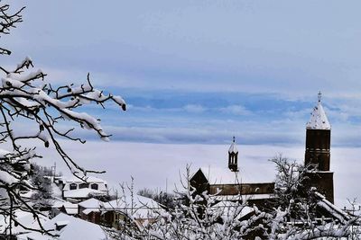 Bare trees on snow covered landscape against sky