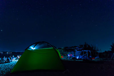 People sitting by illuminated tent against sky at night