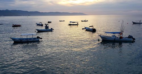 Boats moored in sea against sky during sunset