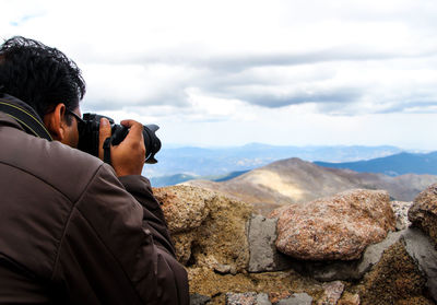 Rear view of photographer photographing mountains against sky