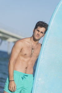 Portrait of shirtless man standing with surfboard at beach