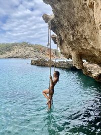 Full length of shirtless man standing on rock in sea