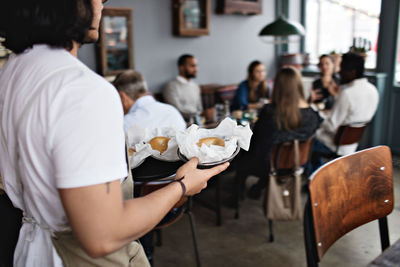 Young waiter serving burgers while walking by customers in restaurant