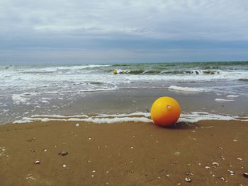 Orange ball on beach against sky