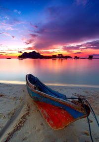 Boat moored on beach against sky during sunset