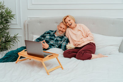 Full length of man using smart phone while sitting on bed at home