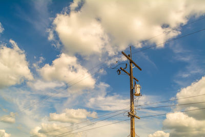 Low angle view of electricity pylon against cloudy blue sky