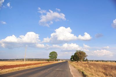 Empty road amidst field against sky