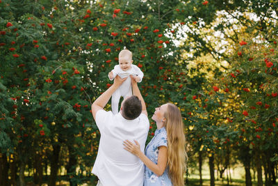 A father and mother play with their son in the park in the summer. a man holds a little boy up