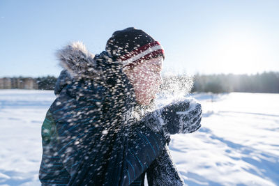 An 11-year-old boy blows snow from his palms in a winter park on a walk in winter.