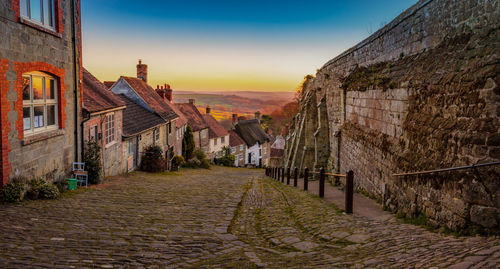 Street amidst buildings against sky during sunset